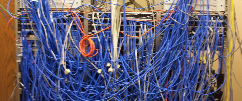 A network cabinet with hundreds of blue cables tangled across the front of the racks
